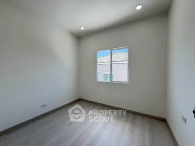 Bright empty room with wooden flooring and a window offering natural light, ideal for customization.