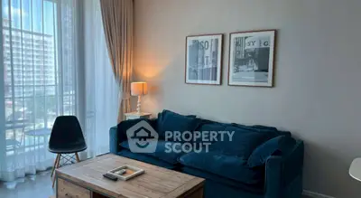 Chic living room with plush blue sofa, stylish decor, and natural light from large windows.
