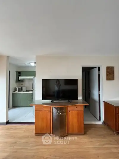 Spacious living room with modern kitchen and wooden flooring, featuring a large TV and stylish cabinetry.