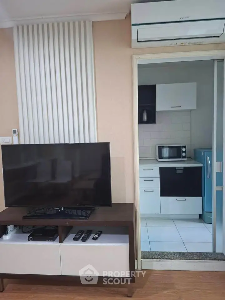 Modern living room with TV and view into compact kitchen with appliances.