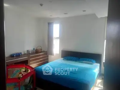 Bright bedroom with blue bedding and natural light, featuring a dresser and a playpen.