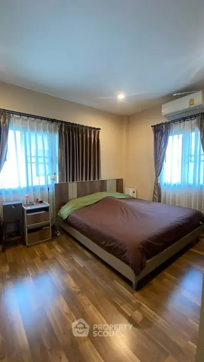 Spacious bedroom with wooden flooring and large windows for natural light