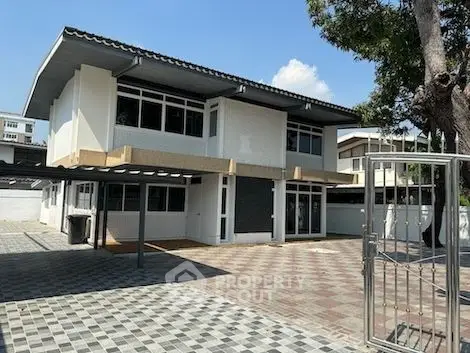 Spacious two-story home with large windows and ample parking, set in a serene neighborhood with mature trees and a welcoming entrance.