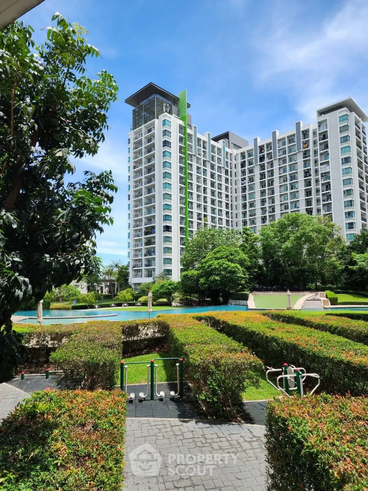 Modern high-rise building with lush garden and pool view under clear blue sky.