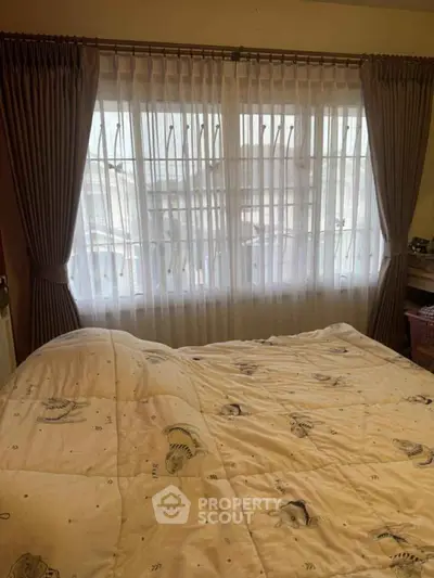 Cozy bedroom with large window and elegant curtains, inviting natural light.