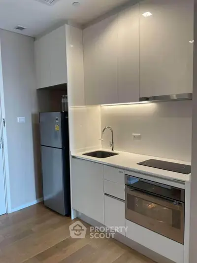 Modern kitchen with sleek cabinetry, built-in oven, and compact fridge in a stylish apartment.