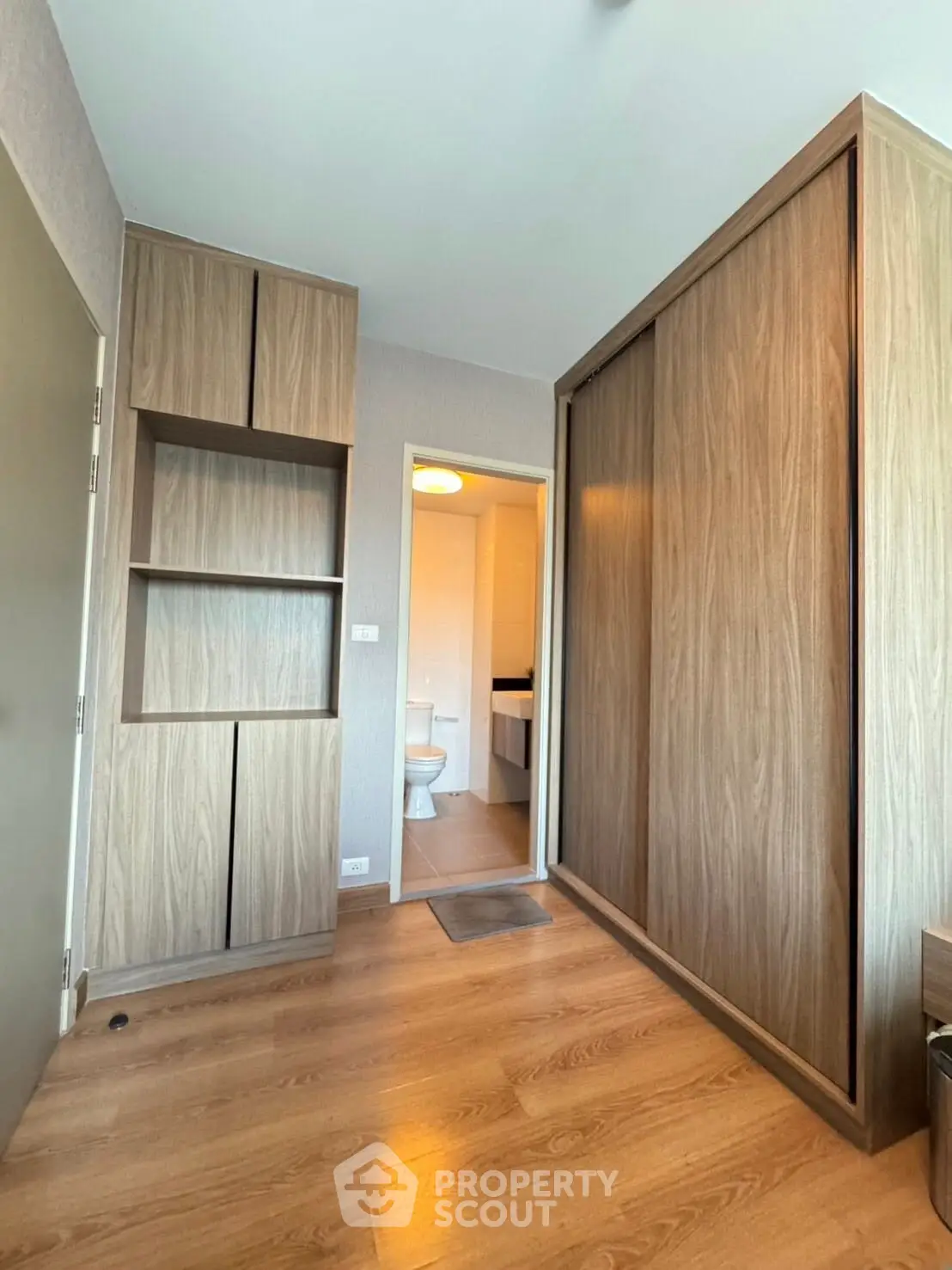 Modern bedroom with wooden flooring and built-in wardrobe, leading to a bathroom.