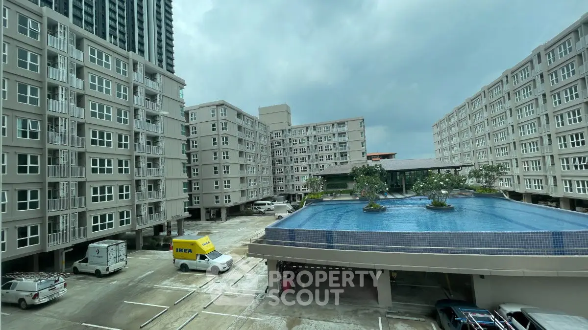 Modern apartment complex with large rooftop pool and parking area.
