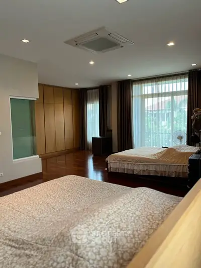 Spacious bedroom with large windows and wooden flooring, offering a serene and elegant ambiance.