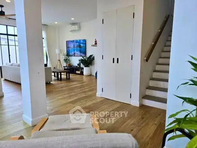 Spacious modern living room with wooden flooring and staircase, featuring stylish decor and ample natural light.