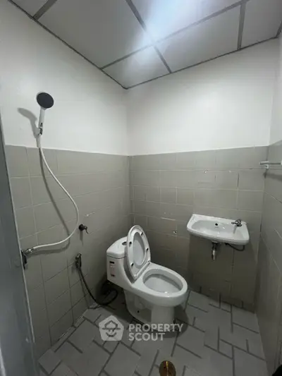 Compact bathroom with shower, toilet, and sink in a tiled setting.