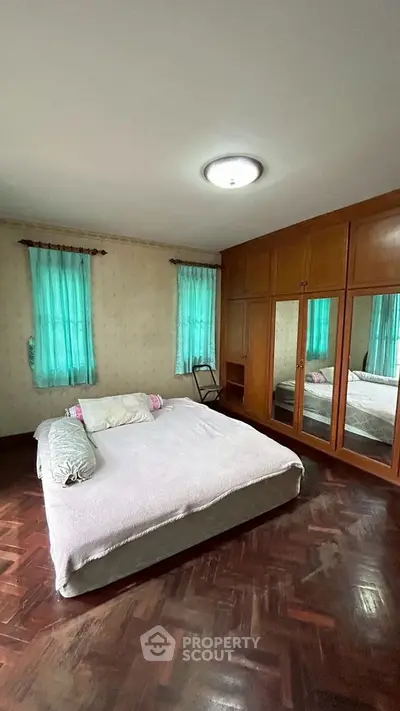 Cozy bedroom with wooden flooring and built-in wardrobe, featuring natural light from two windows.