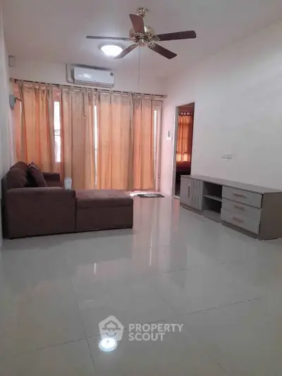 Spacious living room with modern sofa and ceiling fan, perfect for relaxation.