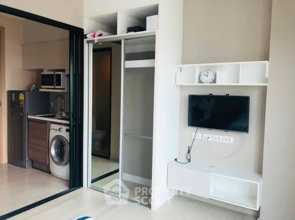 Modern apartment interior with open kitchen and living area featuring washing machine and TV setup.
