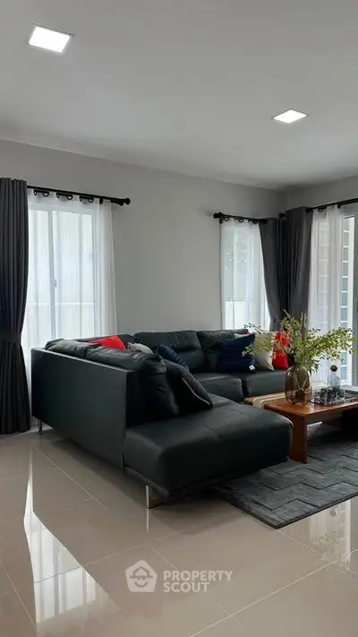 Modern living room with sleek black sofa and elegant decor, featuring large windows and stylish curtains.