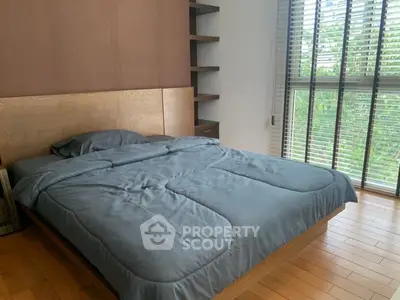 Cozy bedroom with wooden flooring and large window offering natural light.