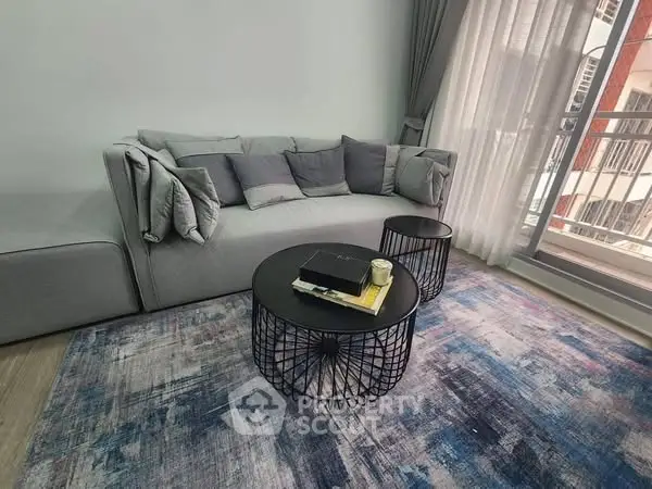Modern living room with stylish gray sofa and chic round coffee tables on a colorful rug.