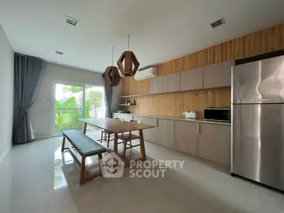 Modern kitchen with sleek cabinetry, stainless steel fridge, and wooden dining table.