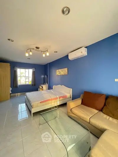 Spacious bedroom with blue walls, cozy sofa, and modern lighting in a bright apartment.
