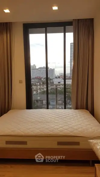 Modern bedroom with large window offering city view, featuring a comfortable bed and elegant curtains.
