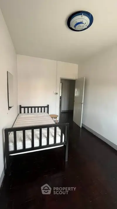 Minimalist bedroom with single bed and dark wooden flooring, ideal for cozy living.