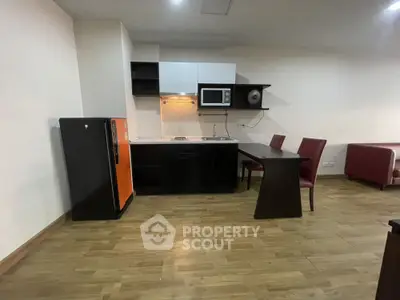 Modern kitchen with sleek black cabinets, compact fridge, and dining area in open layout.