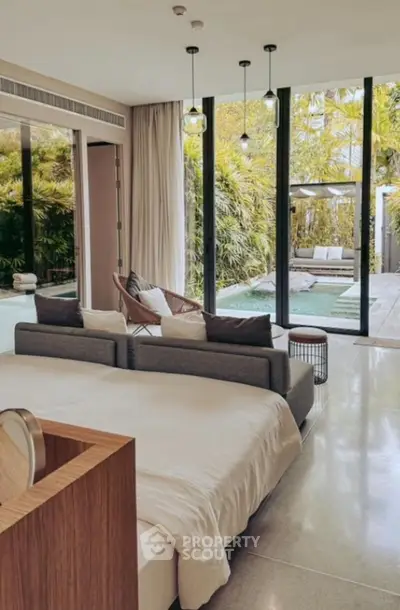Luxurious bedroom with pool view and modern decor, featuring floor-to-ceiling windows and lush greenery.
