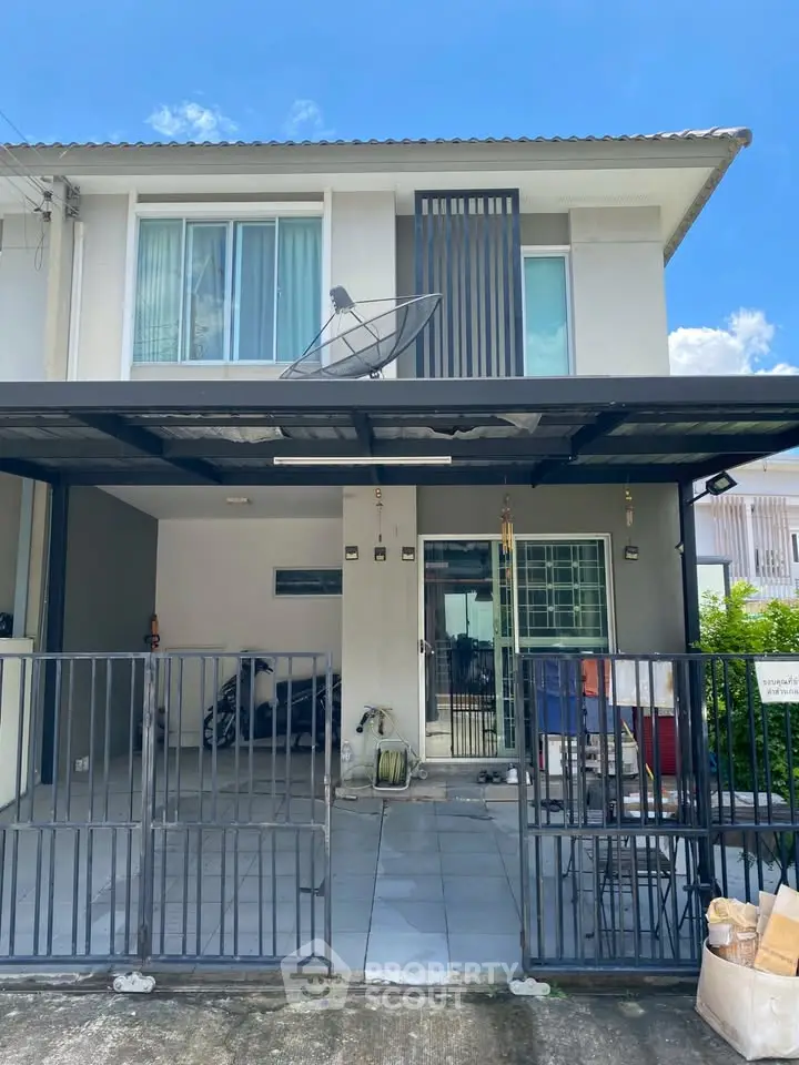 Modern two-story house with gated driveway and satellite dish, perfect for family living.