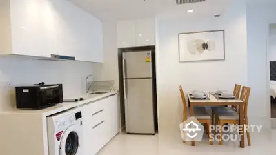 Bright and modern kitchen with open layout, featuring stainless steel appliances, including a refrigerator and washing machine, and a cozy dining area.