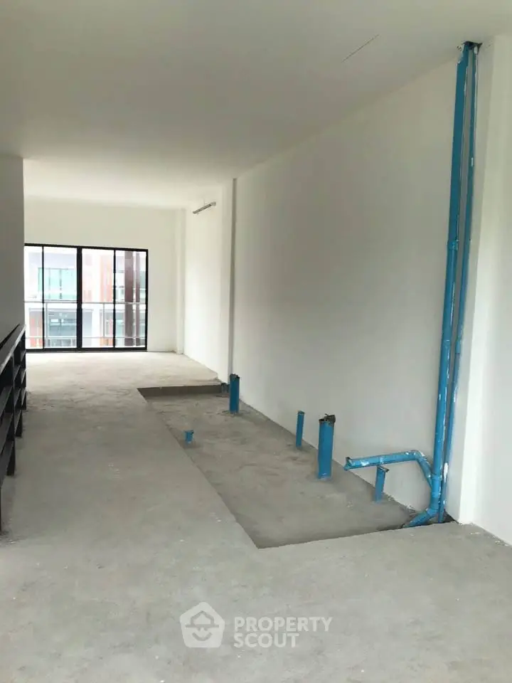 Spacious unfinished apartment interior with large windows and plumbing setup.
