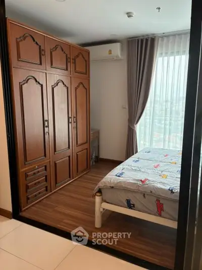 Cozy bedroom with wooden wardrobe and large window offering natural light and city view.