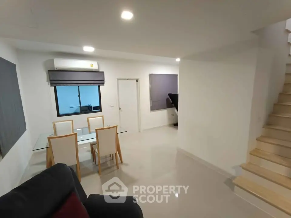 Modern dining area with glass table and wooden chairs in a bright, open-plan living space.