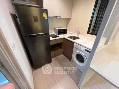 Modern compact kitchen with fridge, washing machine, and microwave in a stylish apartment.