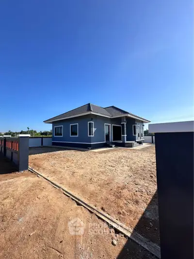 Modern single-story house with spacious yard and sleek design under clear blue sky.