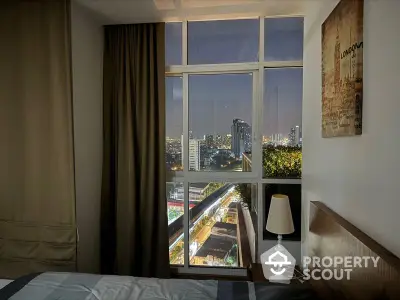 Cozy bedroom with large windows offering a stunning city view, complemented by warm lighting and tasteful decor, perfect for urban living.