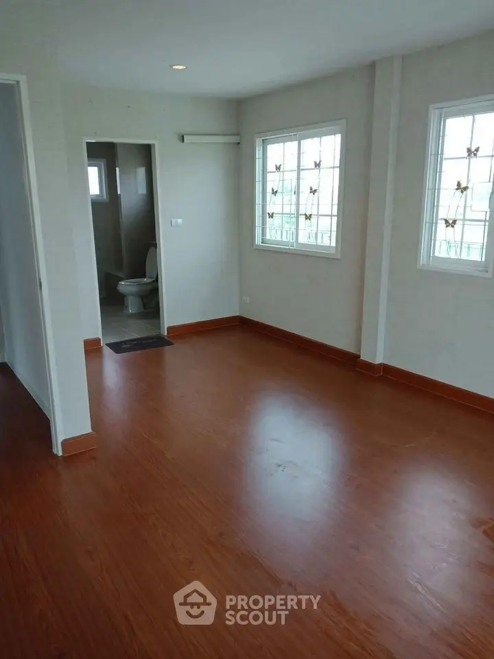 Spacious empty room with wooden flooring and natural light, adjacent to a bathroom.