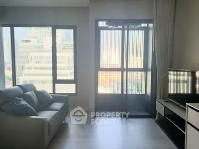 Modern living room with large windows and city view, featuring a sleek sofa and flat-screen TV.
