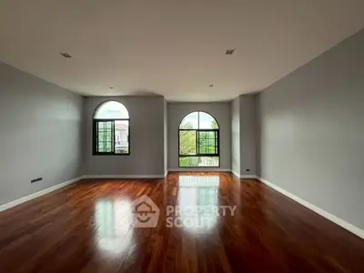 Spacious empty room with elegant wooden flooring and large arched windows offering natural light.