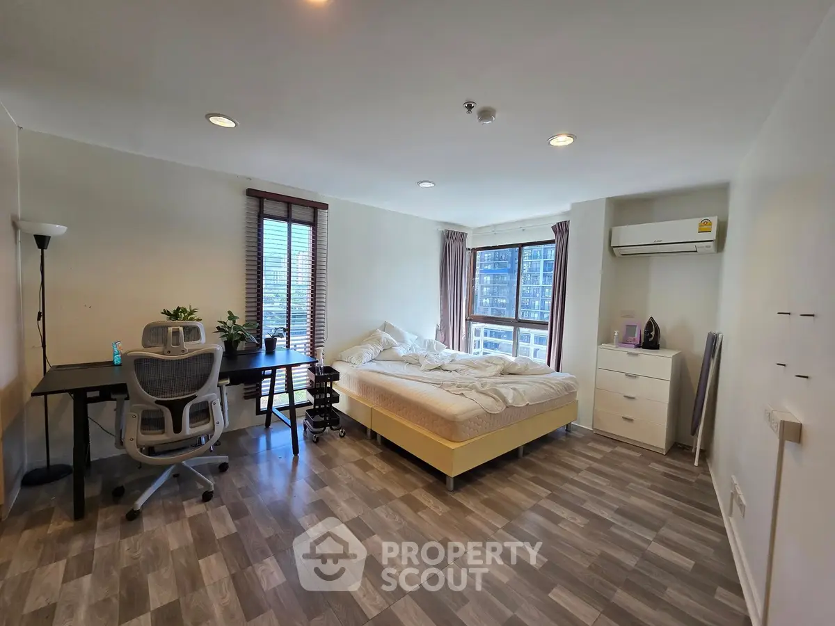 Spacious bedroom with modern decor and city view, featuring a work desk and air conditioning.