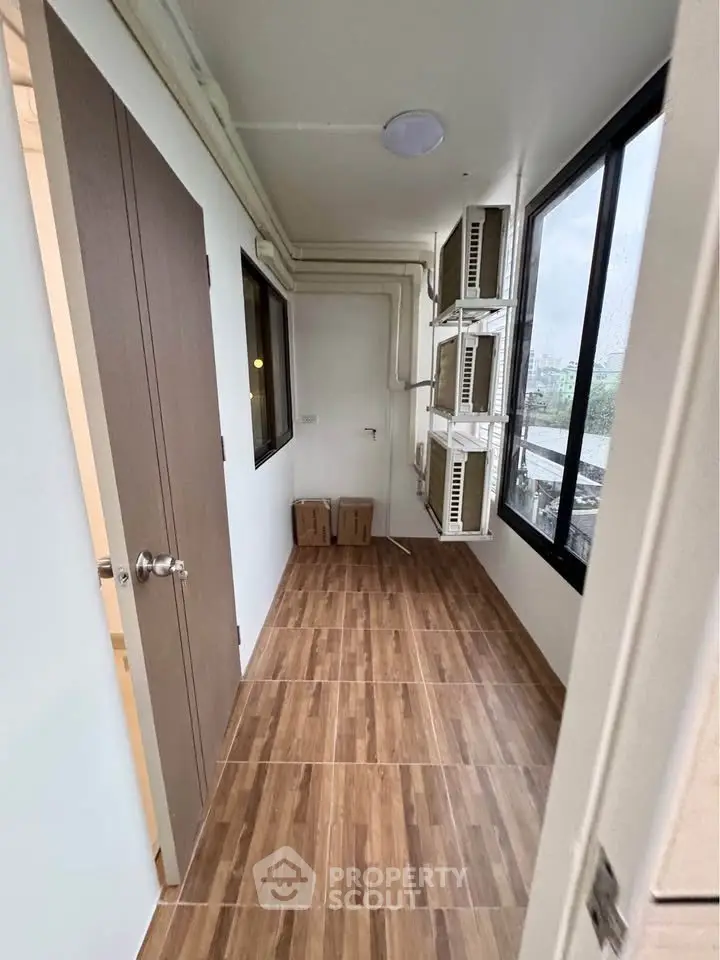 Compact storage room with wooden flooring and large windows in modern apartment.