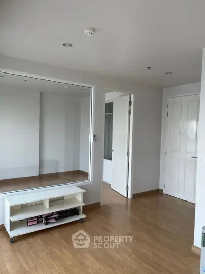Spacious empty room with wooden flooring and large mirror, ideal for customization.