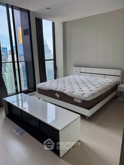 Modern bedroom with city view, featuring sleek furniture and large windows for natural light.