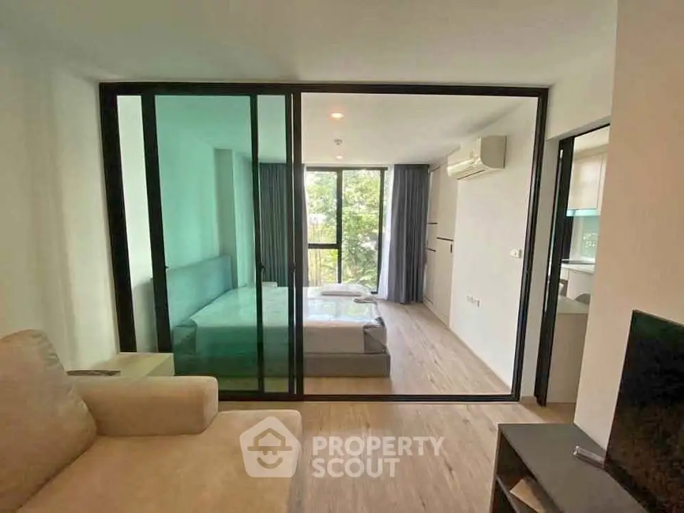 Modern apartment interior with glass partition, cozy living area, and bedroom with large window view.