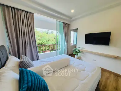 Spacious bedroom with balcony and modern decor, featuring a wall-mounted TV and lush greenery view.