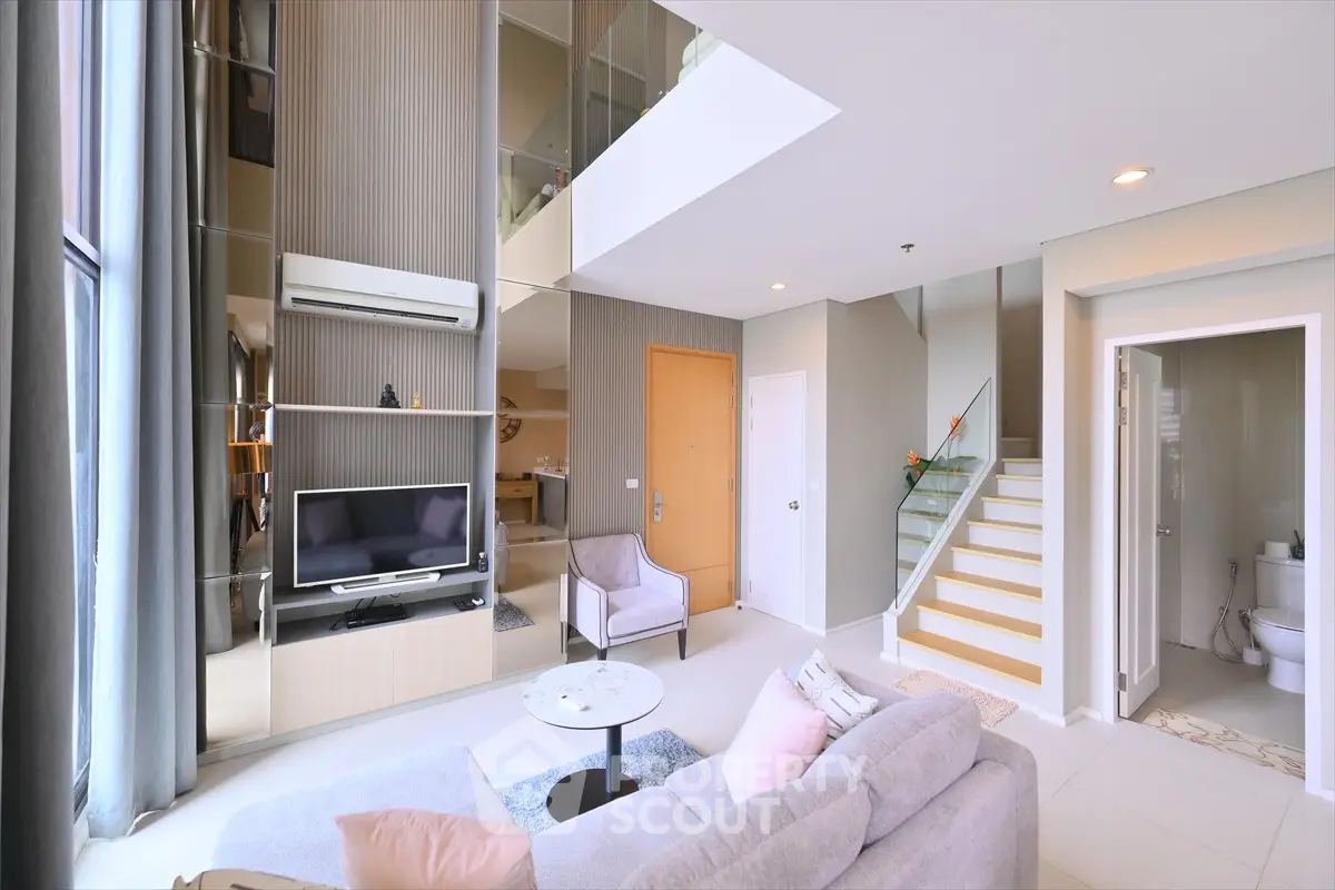 Spacious modern living room with high ceilings and elegant staircase in a stylish apartment.