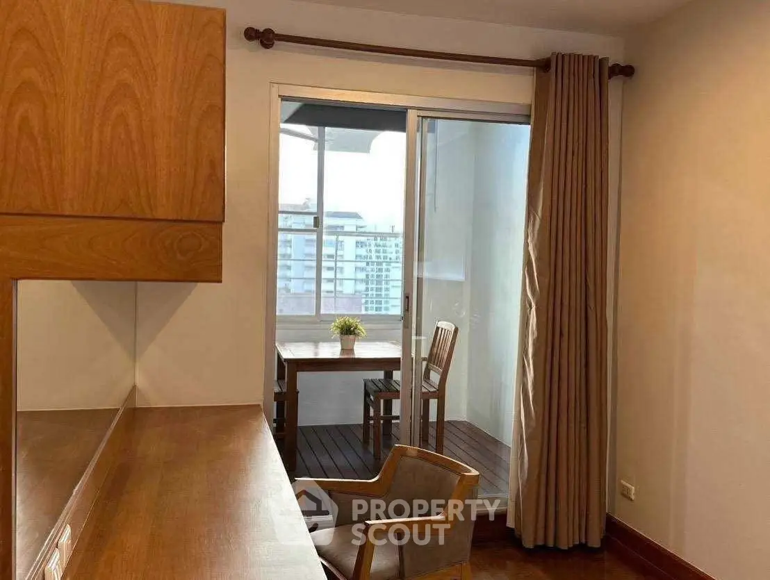 Cozy study room with wooden furniture and access to a small balcony with city view.