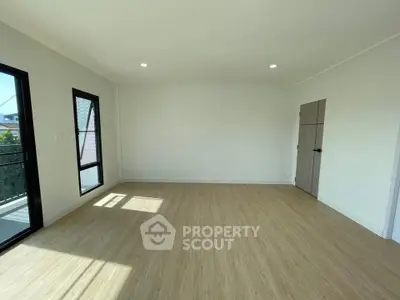 Spacious empty room with wooden flooring and large windows offering natural light.
