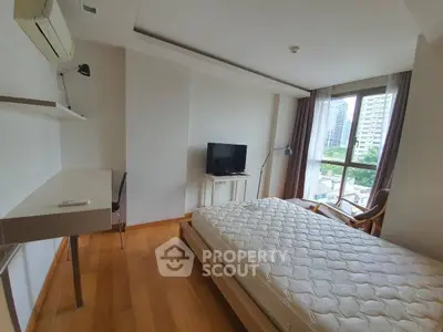 Modern bedroom with large window and city view, featuring a comfortable bed and sleek desk area.