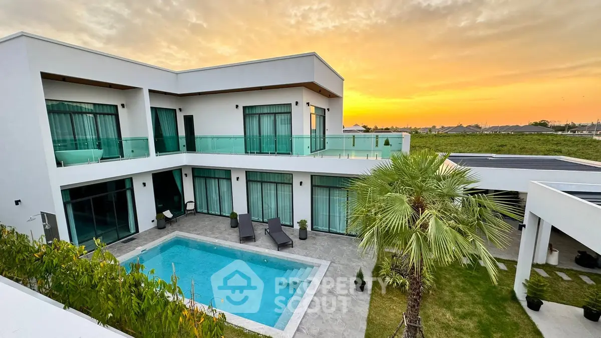 Luxurious modern villa with private pool and sunset view, featuring expansive glass windows and lush landscaping.