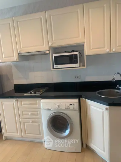 Modern kitchen with white cabinetry, built-in microwave, and washing machine under black countertop.